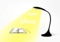 Black modern table lamp, a book, a glasses and a pencil on the table. In the light of the lamp text New ideas