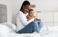 Black mom sitting on bed with her cute infant baby Royalty Free Stock Photo