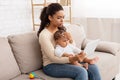 Black Mother With Sick Baby Using Tablet Sitting At Home