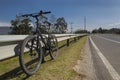 A black mountain bike lying to a Highway metal security fence near to a asphalt highway with green trees, blue sky and sunny day a