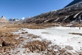 Black mountain witn snow and below with tourists on the ground with brown grass, snow and frozen pond in winter at Zero Point.