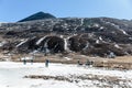 Black mountain witn snow and below with tourists on the ground with brown grass, snow and frozen pond in winter at Zero Point. Royalty Free Stock Photo