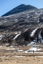 Black mountain witn snow and below with tourists on the ground with brown grass, snow and frozen pond in winter at Zero Point. Royalty Free Stock Photo