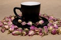 A black mug with a saucer with tea made from dried buds and petals of a purple damask rose stands on a paper background Royalty Free Stock Photo