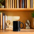 Black mug on wooden shelf with books and decorative objects in warm light indoor setting scene view Royalty Free Stock Photo