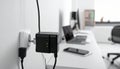 Black multi-port USB charger plugged into a white wall socket with office desk in background Royalty Free Stock Photo