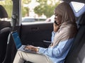 Black muslim businesswoman using laptop and cellphone in car, going to work Royalty Free Stock Photo