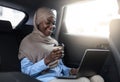Muslim businesswoman working on laptop in car and drinking coffee on backseat Royalty Free Stock Photo