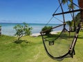 Black net relaxing swing chair on green grass next to a white sand beach with crystal clear waters and palm trees in Fiji