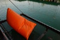 A black net seat with orange pillow to relax over a green pond.