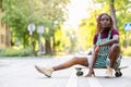 Black non-binary person with a skateboard sitting on the street