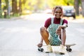 Black non-binary person with a skateboard sitting on the street