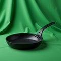 A black, non-stick frying pan with a long handle rests on a lush green fabric backdrop. Royalty Free Stock Photo
