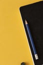 Black notebook with blue pencil next to a removable guitar-shaped disc on a yellow table. Royalty Free Stock Photo