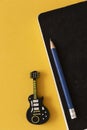 Black notebook with blue pencil next to a removable guitar-shaped disc on a yellow table. Royalty Free Stock Photo