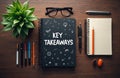 Black notebook with Key Takeaways text and doodles. Desk items include pens, glasses, plant, and open notepad. Concepts for Royalty Free Stock Photo