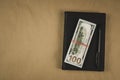 A black notebook , a pen and dollar cash banknotes on wooden background - concept of financial management or planning, make money