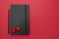 Black notebook on red background with two hearts. Table top for a love, Valentine's Day message