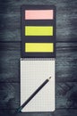 Black notebook with a sheet in a cage with pencil and colored sticky notes on a wooden rustic background, top view Royalty Free Stock Photo