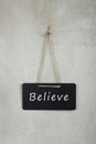 Black notice board, blackboard, chalkboard with text Believe on grey cement wall Royalty Free Stock Photo