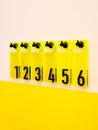 Black numbers one to six on yellow plexiglass plates hang on the wall on black hooks