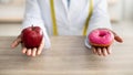 Black nutritionist holding donut and apple, offering choice between fresh and unhealthy foods, sitting at workplace Royalty Free Stock Photo