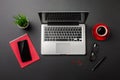 Black office desk table with blank screen laptop computer, notebook, mobile phone and red cup of coffee