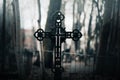 A black old Catholic cross stands in an abandoned cemetery among the trees in the twilight. Horror and fear. Religion and death Royalty Free Stock Photo