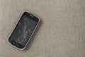 Black old cellphone with cracked screen on light cloth copy space background. Gadget repair and maintenance concept Royalty Free Stock Photo