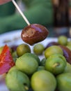 Black Olive caught with a toothpick from spiced olives plate on tapas bar table typical Spanish green split variety