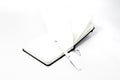 Black open small notepad, gel pen lie in unfold large notebook, note with blank light pages. White backdrop Royalty Free Stock Photo