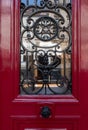 Black ornate gratings of old wooden door frame painted in wine red color. Blurry reflection in door window glass Royalty Free Stock Photo