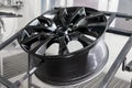 A black painted aluminum alloy wheel is mounted on a special frame during drying in a chamber in a vehicle body repair workshop. Royalty Free Stock Photo