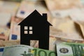 A black paper house with euro banknotes in background