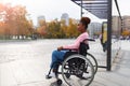 Black paraplegic woman in wheelchair waiting on bus stop, cannot board vehicle suitable for handicapped persons