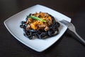 Black pasta with cuttlefish ink. Pasta of durum wheat semolina with squid ink with beef and sweet pepper sauce on a square plate