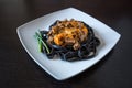 Black pasta with cuttlefish ink. Pasta of durum wheat semolina with squid ink with beef and sweet pepper sauce on a square plate