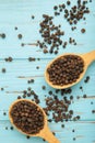 Black pepper corns in wooden spoon on blue wooden background. Vertical photo Royalty Free Stock Photo