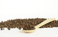 Black pepper and wooden spoon on white background. Spoon in front of heap of grains of pepper. Sample for Spice packing