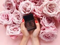 Black perfume spray bottle, female hands with red nails and pink roses flowers a lot. Blank label bottle for branding.  Eau de Royalty Free Stock Photo