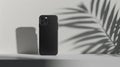A black phone case standing on a white surface with a shadow of a leaf behind it on the wall Royalty Free Stock Photo