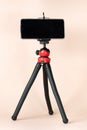 A black phone tripod stands on a light pink background.