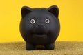 Black piggy bank standing on yellow, gold sand in front of yellow background