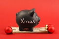 Black piggy bank with text Xmas standing on stack of money american hundred dollar bills and three red matt christmas balls