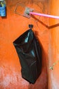 A black plastic bag hangs as an improvised trash bin against a worn, rustic orange wall in a simple interior setting. Royalty Free Stock Photo