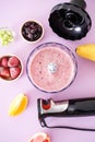 Black plastic electric hand blender and accessories with fruits and smoothie ready on purple background, vertically. Flat lay Royalty Free Stock Photo