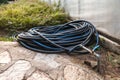 A black plastic hose with a blue stripe is twisted into rings and connected to a water pipe on the backyard Royalty Free Stock Photo