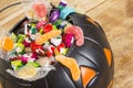 Black plastic pumpkin filled with candy on wooden table