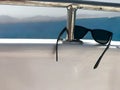 Black plastic sunglasses hang on an iron railing on a yacht against the blue sea and mountains