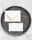 Black plate with a blank card, envelope and wto wedding rings top view, mockup